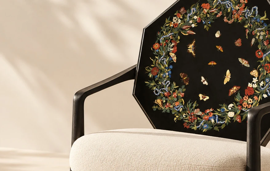 A sculptural chair with a black stone backrest decorated with an intricate floral inlay and a cream upholstered seat.